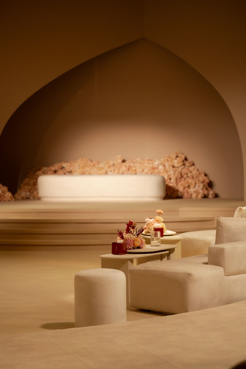 An ivory sofa before a bank of blush hydrangea in a pointed arch alcove, low lounge tables with flowers in front